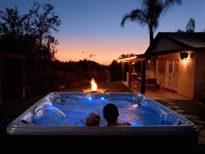 Couple relaxing in a Hot Spring Spas hot tub under a starry sky, enjoying the benefits of aromatherapy and a tranquil evening.