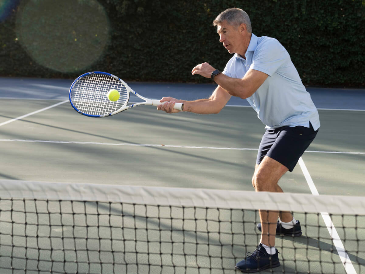 A man in a light blue shirt and black shorts hits a tennis ball on an outdoor court.