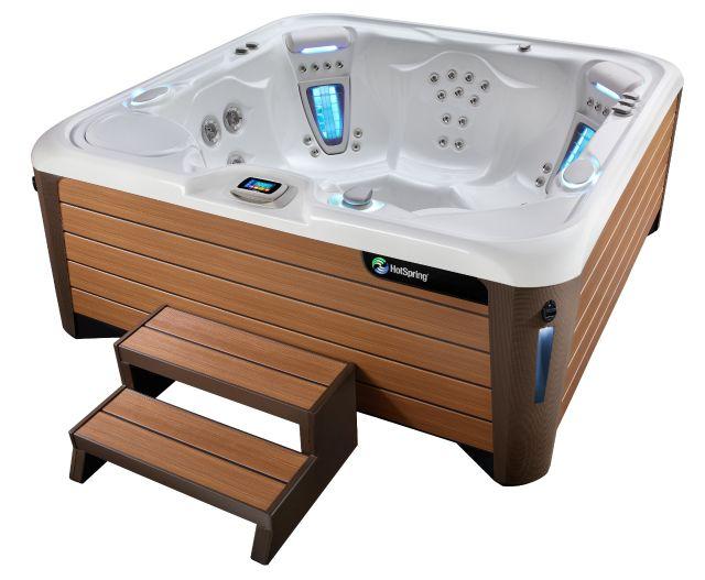 A sleek, modern Hot Spring spa with a wood-look cabinet and a convenient step. The spa features a built-in control panel and illuminated jets.