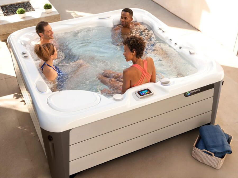 Friends laughing and relaxing in an Aria Alpine White Hot Tub from Hot Spring Spas, enjoying a perfect afternoon.