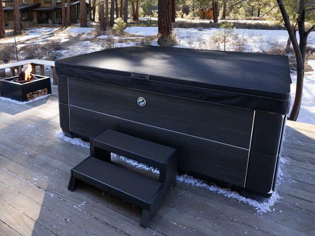 A Hot Spring Spa Grandee hot tub with a snug-fitting Weather Pro™ Cover sits amidst a snowy winter landscape, showcasing the importance of using a cover to winterize a hot tub.